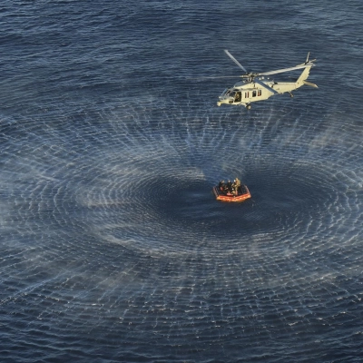 U.S. Navy divers and Artemis II astronauts aboard an inflatable raft are approached by helicopters and lifted away to the...