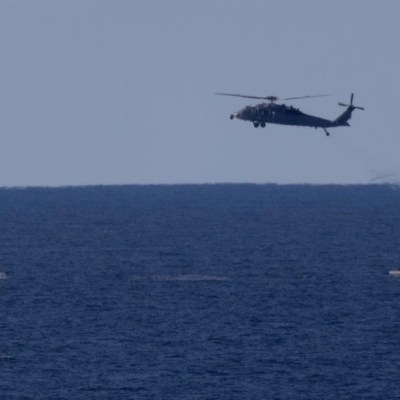 A U.S. Navy MH-60 Seahawks from Helicopter Sea Combat Squadron (HSC) 23 flies overhead as small boats approach NASA’s Orion...