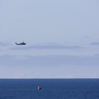 Two U.S. Navy MH-60 Seahawks from Helicopter Sea Combat Squadron (HSC) 23 flies overhead as small boats approach NASA’s Orion...